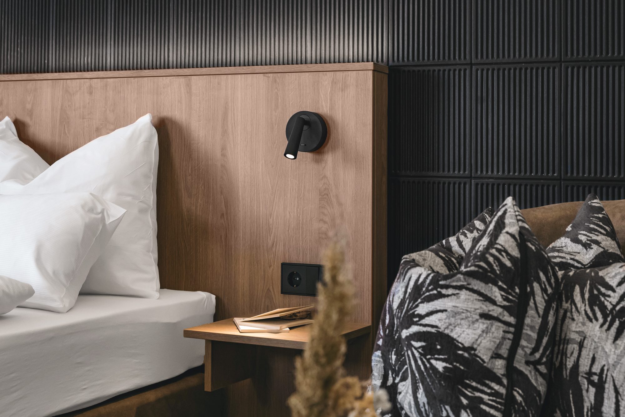 Detail im Zimmer: Kopfteil aus Holz mit Leselampe, Steckdose und kleiner Ablage neben dem Bett