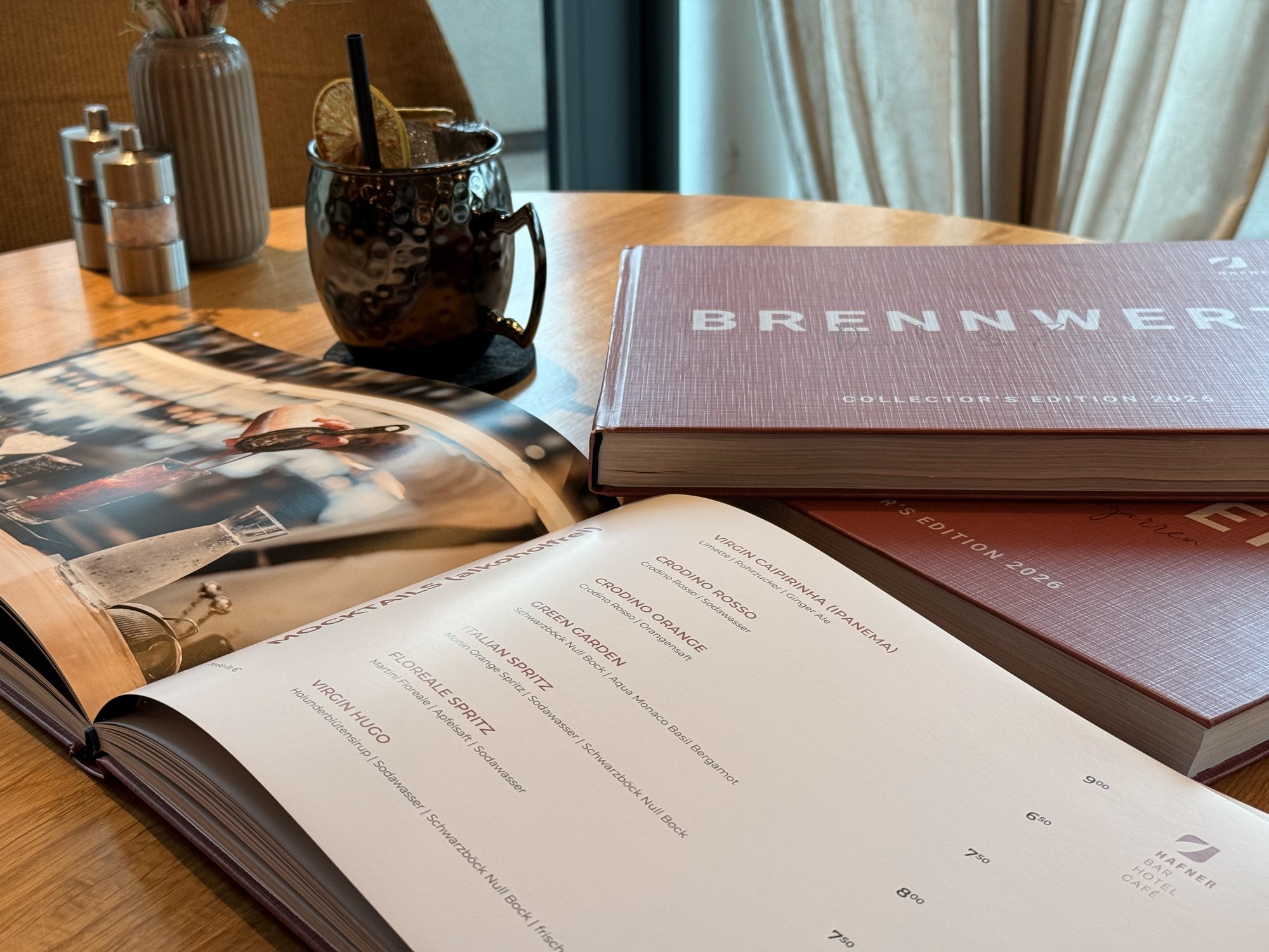Das Barbuch BRENNWERT, aufgeschlagen bei den Mocktails, daneben ein Kupferbecher
