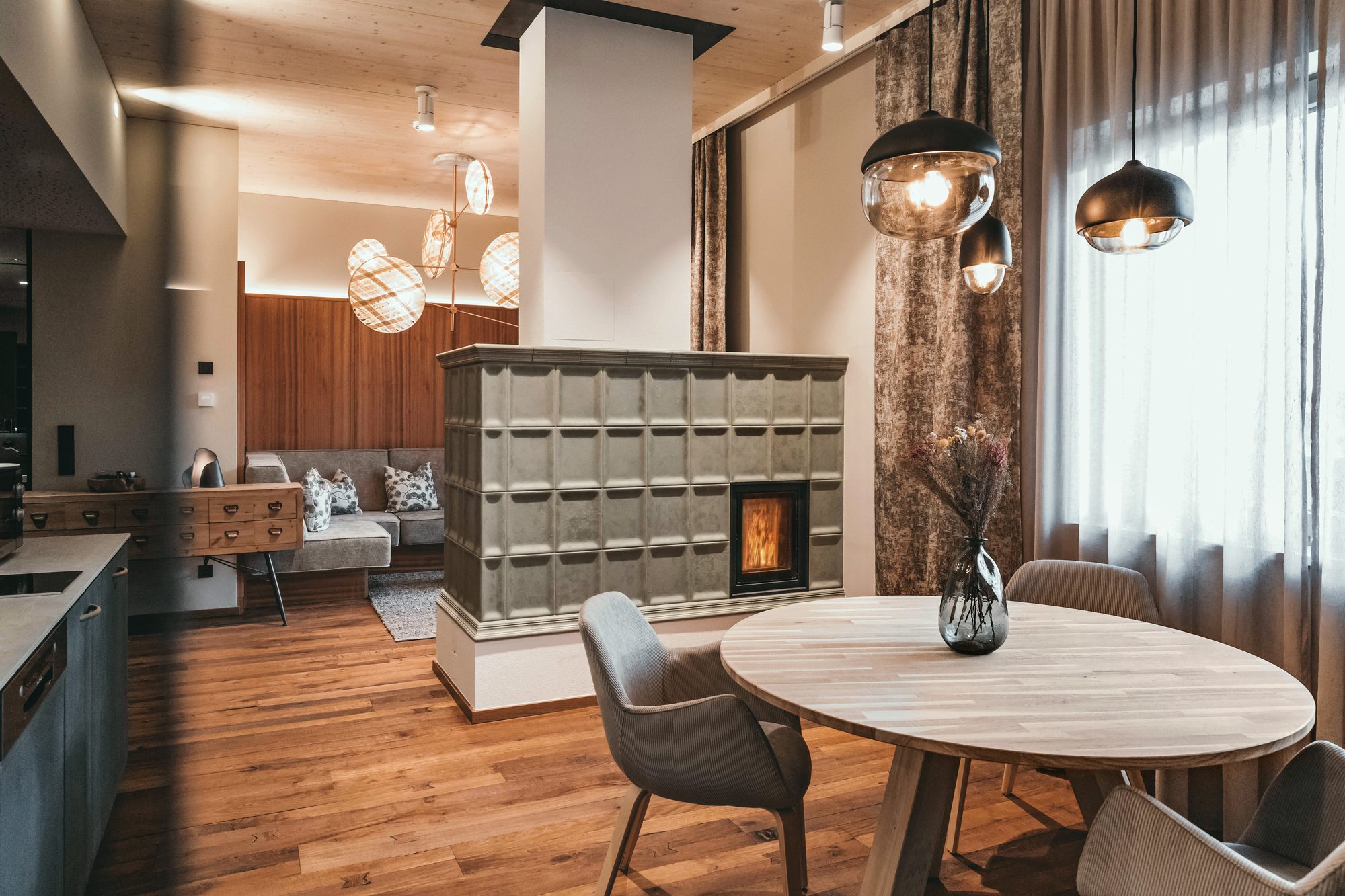 Suite Castello mit 49 m²: hell glasierter Kachelofen mit brennendem Feuer neben dem runden Esstisch