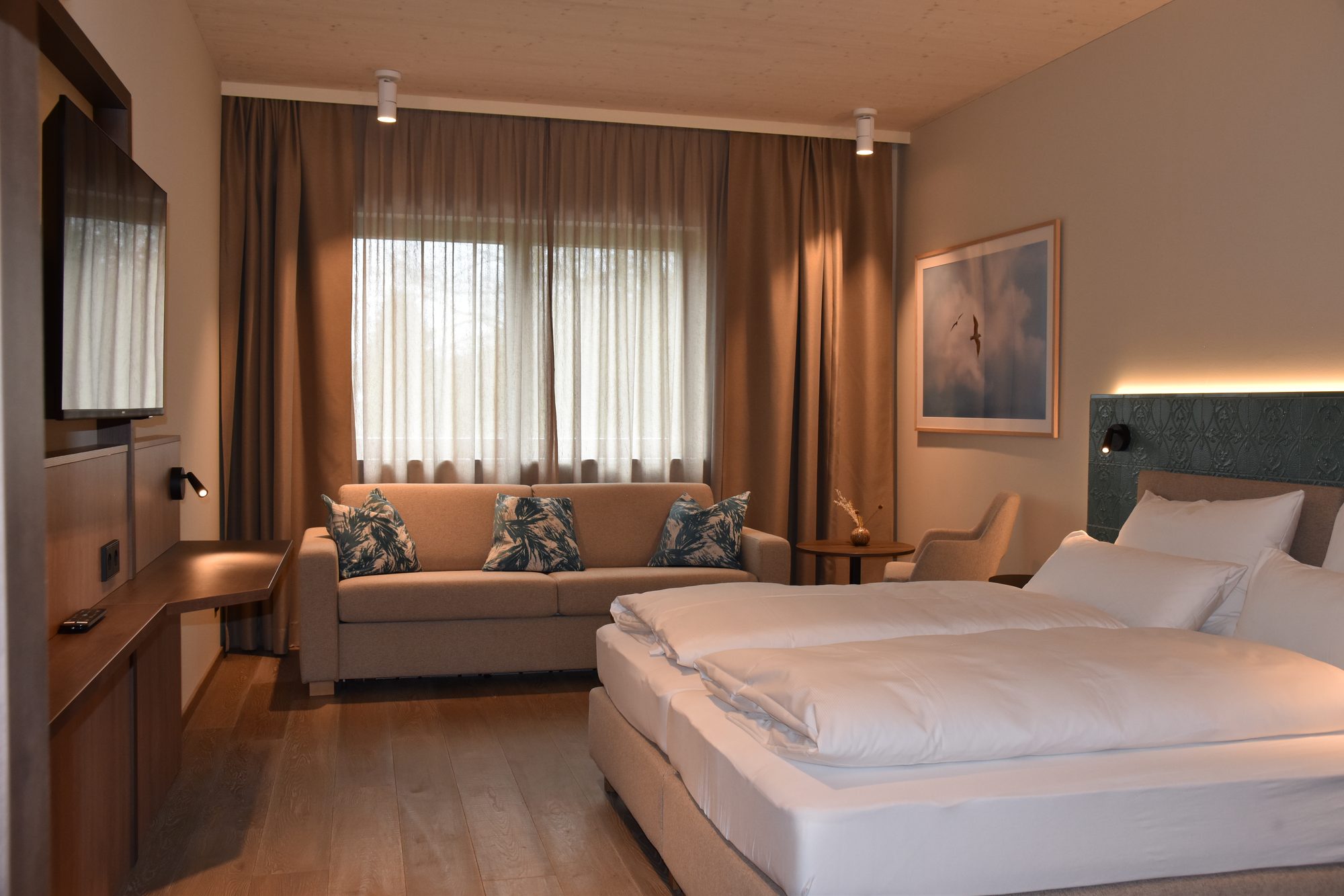 Deluxe-Zimmer mit 30 m²: Doppelbett und Sitzbereich mit Sofa am Fenster