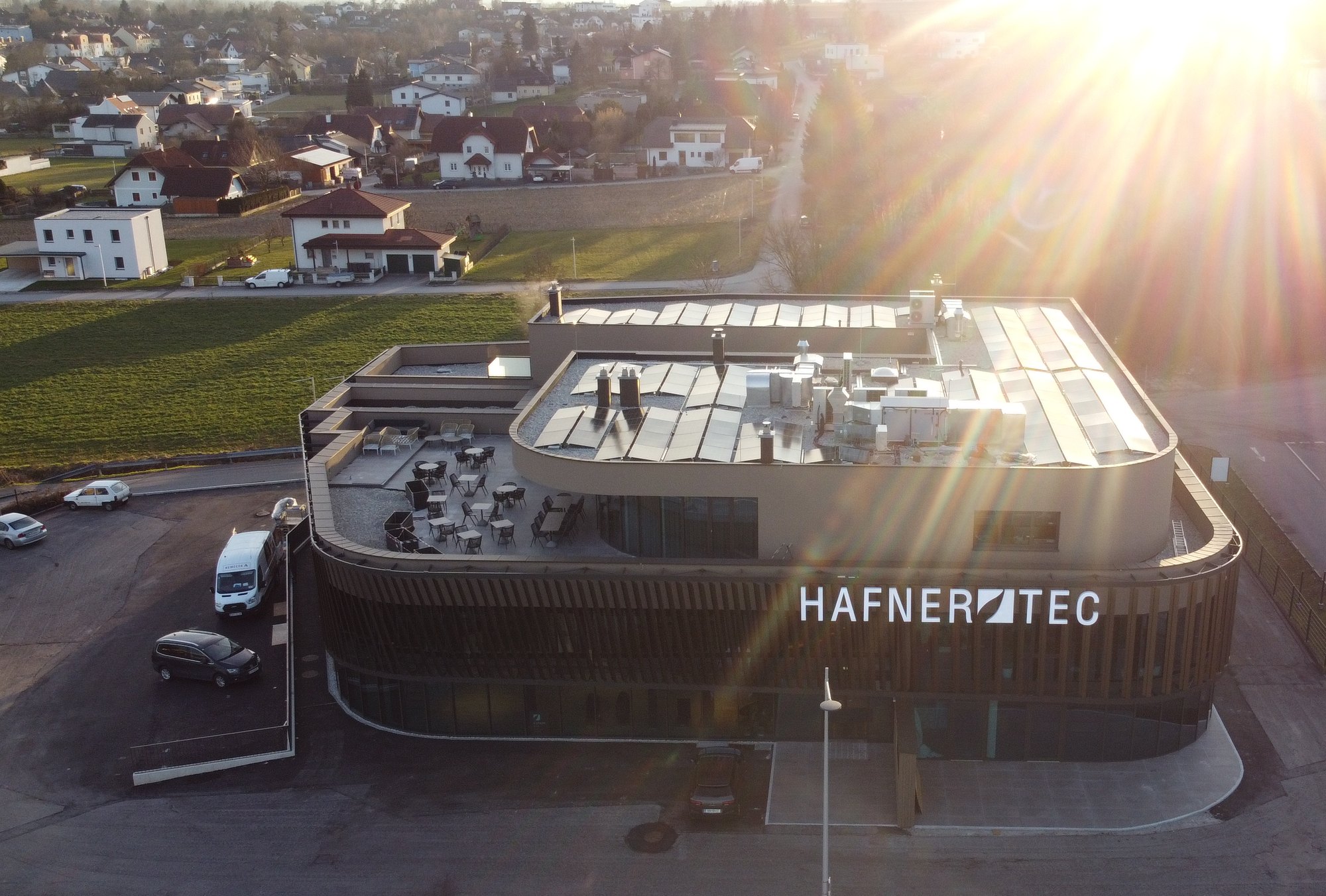 Das Hafnerhotel von oben bei Sonnenuntergang: die Dachterrasse mit Tischen und Stühlen über dem Haus, dahinter Wieselburg