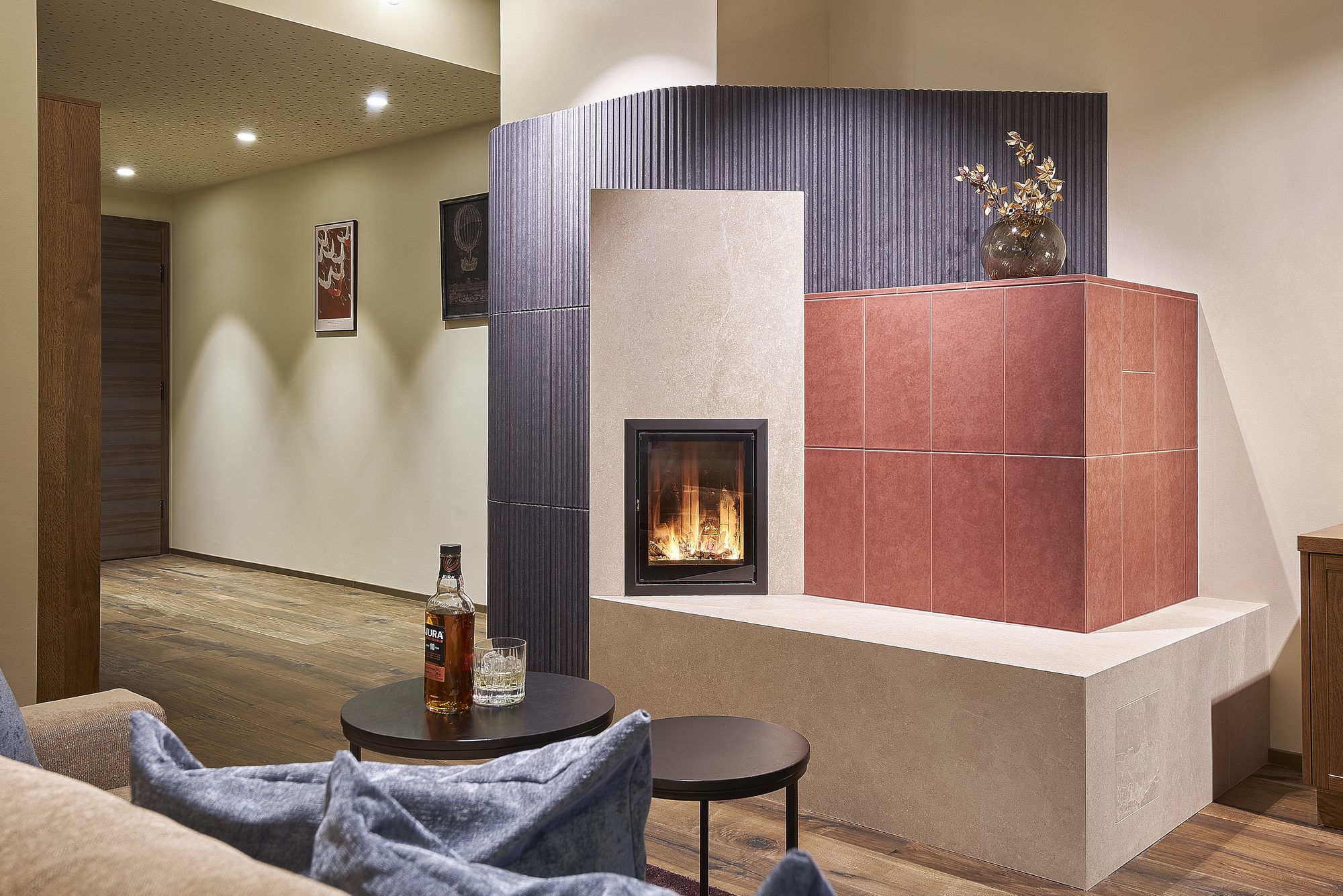 Suite Infinita mit 60 m²: Kachelofen in Terrakotta und Kupfer mit brennendem Feuer, davor der Sitzbereich