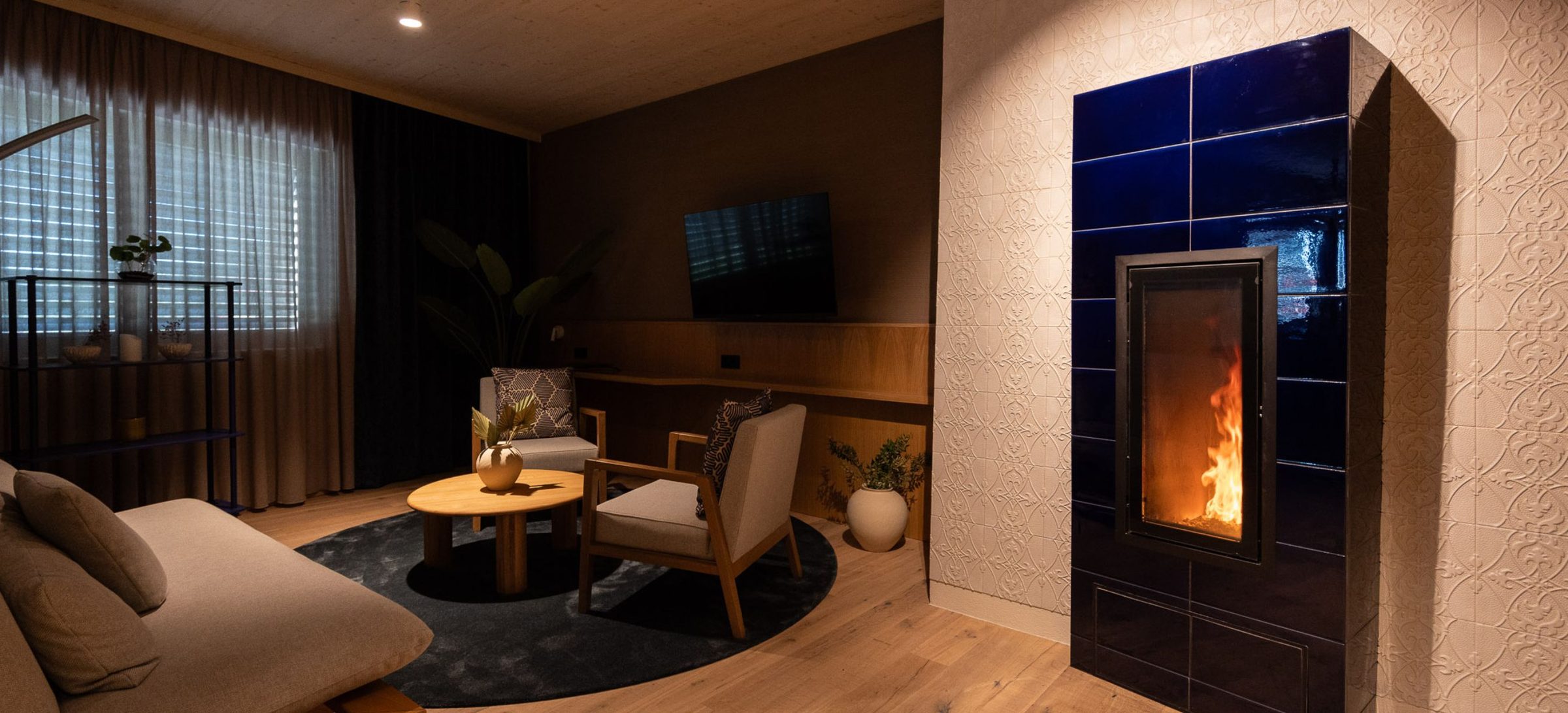 Der tiefblau glasierte Kachelofen der Suite DaVinci mit Feuer, daneben die Sitzgruppe