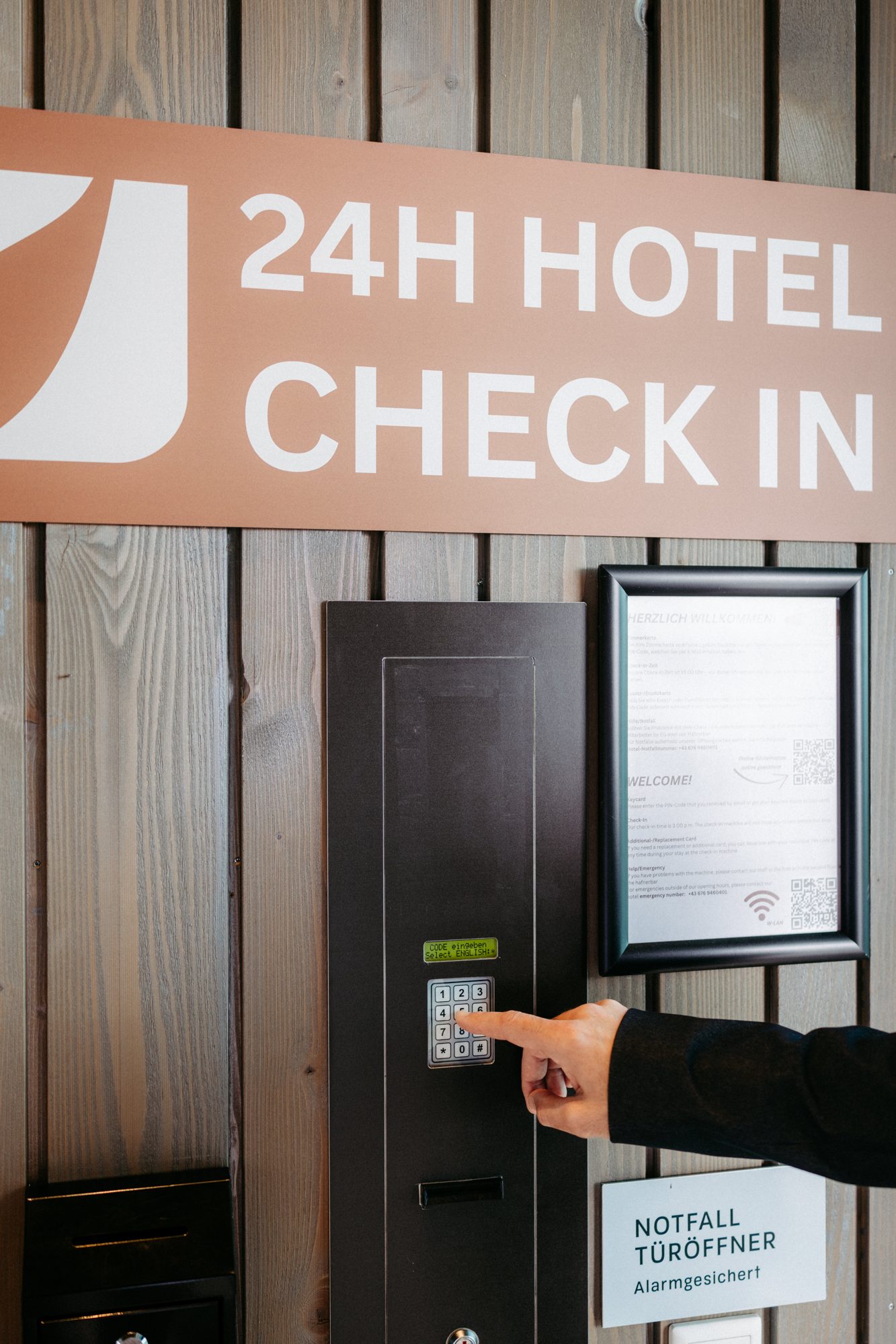 Self-Check-in im Hafnerhotel: eine Hand tippt den PIN am Check-in-Automaten unter dem Schild 24h Hotel Check-in ein